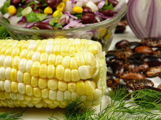 Glass bowl with vegetable salad based on corn, side view. Ingredients. Fresh corn on the cob, red bean, red onion, dill, parsley and green scallions