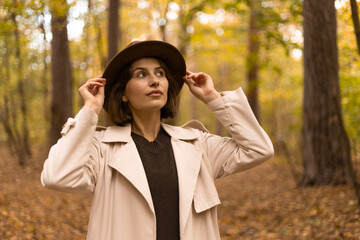 Young woman standing in an autumn park holding her hat with both hands