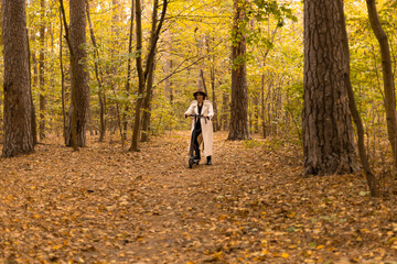 Dynamic shot of a fashionable young woman commuting through the park on a scooter in autumn