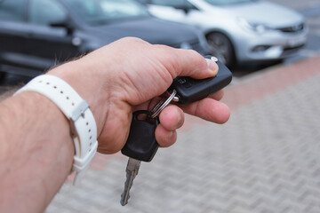 Fototapeta premium Man holds a car key in a parking lot with several cars. The concept of remote car opening and vehicle rental in dealership.
