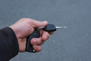 Close-up of a hand holding car keys with a black key fob. Photo for topics about car ownership, vehicle security, transportation and driving.