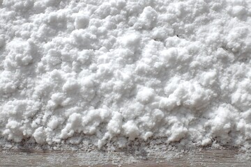 A close-up shot showcasing a pristine white, powdery substance resembling snow or salt, spread across a textured wooden surface, creating a minimalist composition.