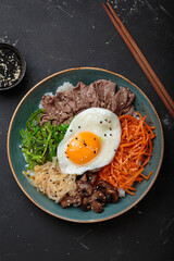 Bibimbap, authentic korean dish with a steamed rice topped with fried egg, beef, colorful vegetables, traditional dish of Korea top view on black background