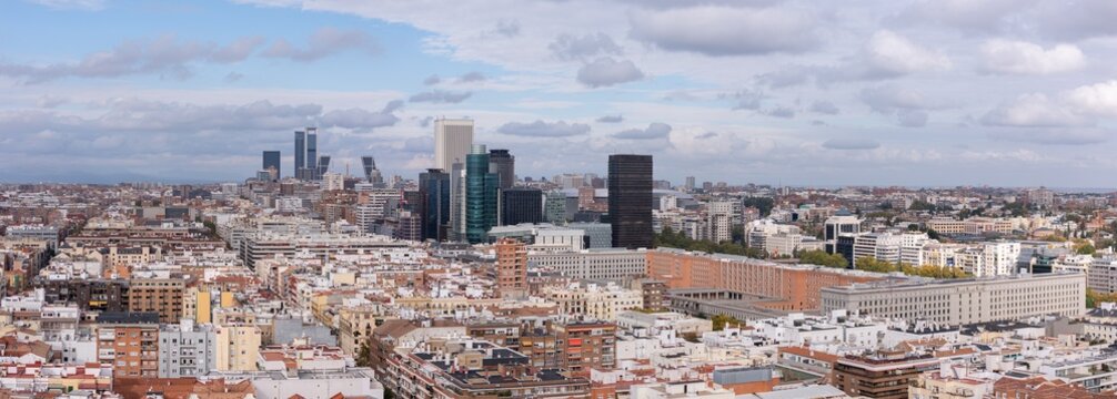 Aerial view of a city's rooftops and modern skyscrapers piercing the skyline under a cloudy sky, Madrid, Spain.