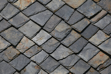 Stone tiles on roof of an old house. Grey and black squares with natural stone texture. Vintage roof
