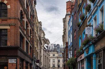Obraz premium A view down a street of Soho in London with a big silver Soho sign suspended above it.