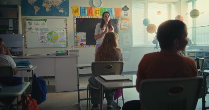Female Teacher Introducing New Young Student in Front of Class Full of Elementary School Children. Group of Diverse Kids Sitting at the Desks, Clapping in Hands, Greeting New Classmate Before Lesson.