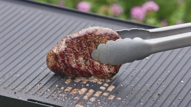 outdoor cooking. cook preparing fresh beef fillet mignon steak with spices on hot grill pan for making delicious meal in garden, food closeup, outdoors natural light