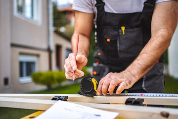 Unrecognizable men measuring wooden plank outdoors