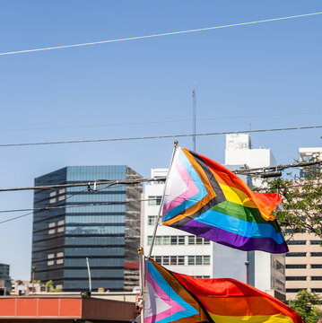Progress pride flags waving in front of urban skyscrapers during LGBTQ event