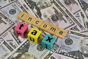 Wooden letter blocks spelling out "income tax" rest on a bed of US dollar bills.