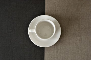 Empty white coffee cup and saucer on a two-toned table.