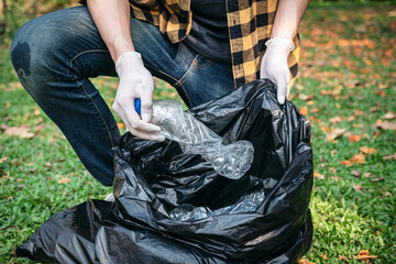 Volunteer man in gloves sitting to squeeze plastic bottles and collect into plastic black bag for cleaning