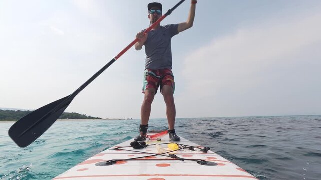 Man falling from stand-up paddleboard into the sea, captured at the exact moment of losing balance. Summer adventure fail in slow motion over crystal clear blue water
