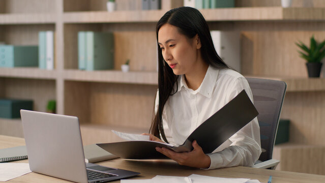 Confident Asian Japanese businesswoman female girl Korean Chinese business woman office worker secretary manager lawyer talk online call laptop remote meeting client analyzing documents folder indoor