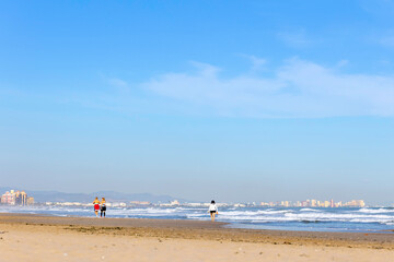 Summer vibes on the sunny autumn beach of Malvarrosa in Valencia, Spain. Vast expanses of smooth fine sand on the sea coast attract vacationers to solitary walks along the bubbling foamy waves.