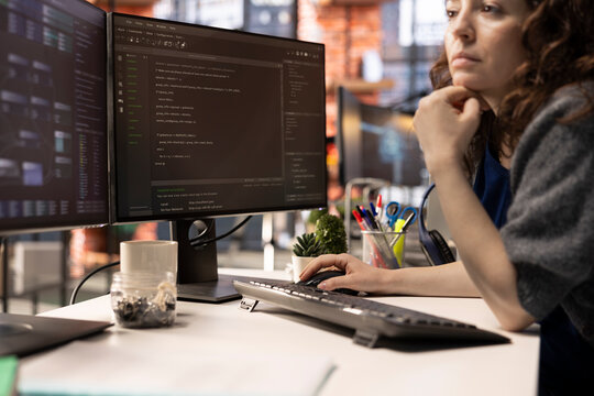 Female programmer seen typing code for a user interface design on dual monitors, working in a digital workspace. Woman IT specialist working on software engineering and front end development.