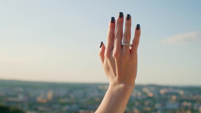 Close up of young female hand with diamond engagement ring princess cut, gold outside outdoors. Woman in nature enjoys beautiful expensive wedding ring. Concept of marriage, jewelry advertising.