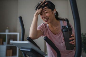 Japanese woman use tablet and hold protein shaker on a exercise bike