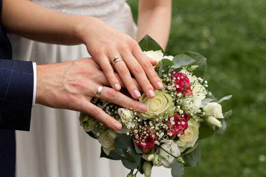 Wedding couple holding hands over bouquet of roses and greenery in a lush outdoor garden setting