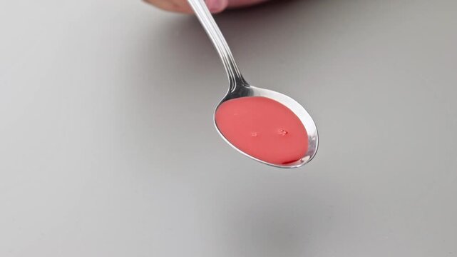 Syrup, a liquid dietary supplement, poured onto a silver tablespoon, for soup. A pink liquid dietary supplement. Dosage and treatment: One serving daily. Micellars and medicine in liquid form.