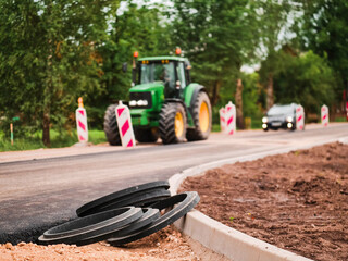 Road works in a rural country side area. Plastic fittings and freshly laid asphalt in foreground, safety security signs and tractor out of focus in the background. © mark_gusev