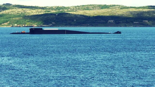 Severomorsk, Russia - Jyly 28, 2019: A nuclear-powered submarine in bright blue water against the backdrop of low mountains in the Kola Bay during the annual Navy Day holiday.