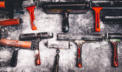 Various inky printmaking brayers and rollers scattered on a textured, paint-dusted surface. A colorful artistic setup showcasing tools used for printmaking, monoprint, or block printing projects.
