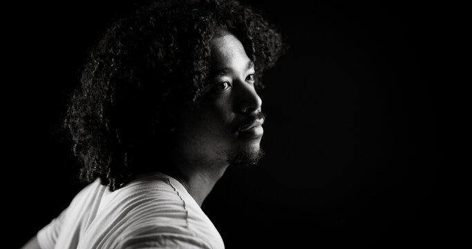 Dramatic black and white portrait of a young african-american man with curly hair looking away from the camera against a dark background