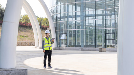 Engineer in High-Visibility Vest Using Digital Device Outside Modern Building