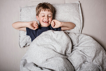 Smiling boy waking up joyfully, stretching arms in bed. Positive morning vibes, happy childhood and...
