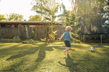 Little boy playing soccer in sunlit backyard