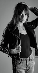 Fototapeta premium Fashionable young woman with long hair wearing leather jacket and jeans posing in studio