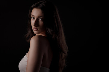 Naklejka premium Studio portrait of beautiful young woman with long brown hair looking over shoulder on black background