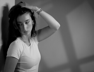 Fototapeta premium Young woman with hand on hair posing near a wall in black and white