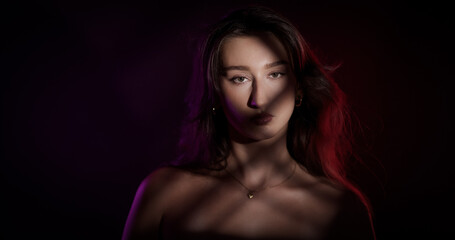 Fototapeta premium Studio portrait of a young woman with colored lights and shadows projected on her face and body