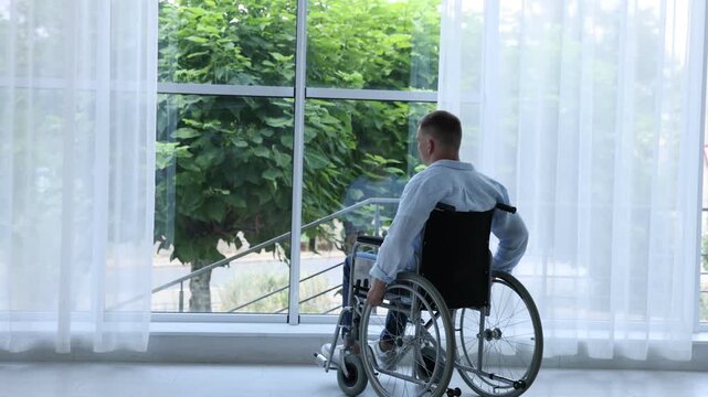 Young man in wheelchair near window indoors