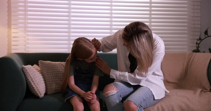 Mother apologizing to her crying daughter on sofa at home