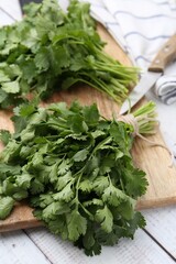 Cutting board with fresh cilantro and knife on white wooden table, closeup