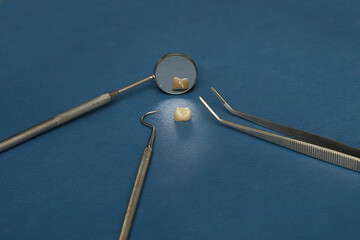 Ceramic dental crown surrounded by mirror, tweezers, and dental probe on blue background. Concept of dental restoration, precision work, and prosthetic treatment.