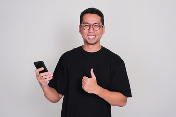Adult Asian man smiling happy and give thumbs up while holding mobile phone