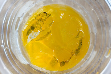 An overhead close-up shot of a refreshing yellow beverage with ice cubes in a clear glass, showing condensation on the outside.
