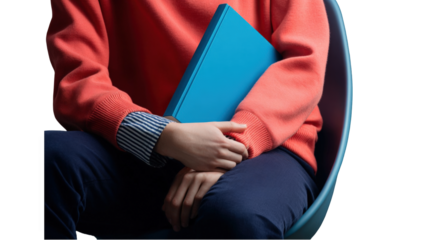 Seated person in a coral knit sweater holding a plain blue hardcover book on their lap.