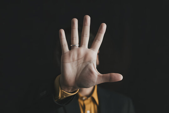 Man holding hand up in stop gesture against dark background person