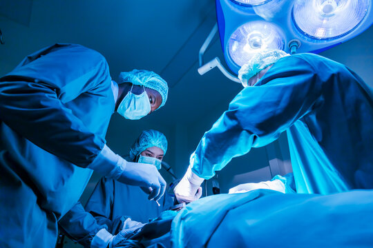 Team of surgeon doctor using defibrillator to give electrical shock to patient heart who is suffering from cardiac arrest in emergency surgical room for healthcare usage