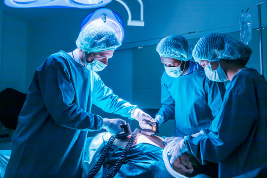 Team of surgeon doctor using defibrillator to give electrical shock to patient heart who is suffering from cardiac arrest in emergency surgical room for healthcare usage