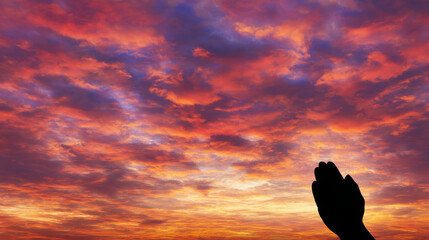 Silhouette of a hand in prayer against a vibrant sunset sky.