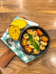 Stir-fried shrimp with basil on a hot pan and Garlic bread is served on the side.