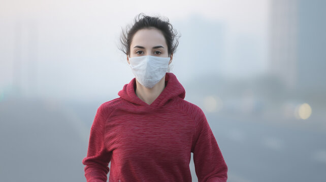 Young woman jogging in polluted city wearing red hoodie and face mask, determined expression, urban morning - Powered by Adobe