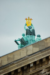 Fototapeta premium Gilded Statue atop Historic Parisian Building Under Overcast Sky. The statues appear to be made of a weathered, green-patina bronze